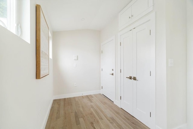 corridor with light wood finished floors, baseboards, and lofted ceiling