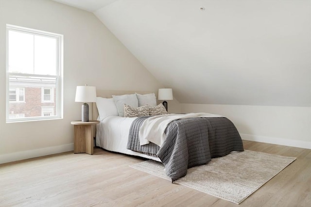 bedroom with baseboards, light wood-type flooring, and vaulted ceiling