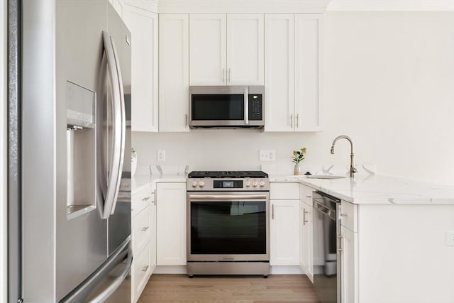 kitchen with stainless steel appliances, a sink, white cabinets, light stone counters, and light wood finished floors