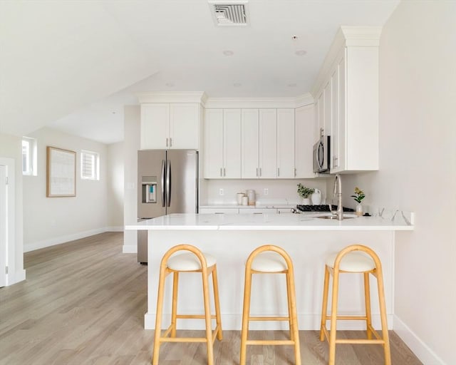 kitchen featuring appliances with stainless steel finishes, a peninsula, light countertops, and a breakfast bar