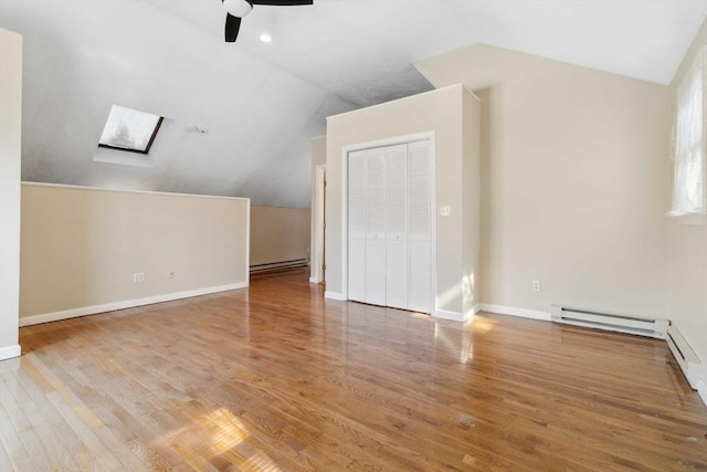 additional living space with a baseboard heating unit, lofted ceiling with skylight, wood finished floors, and baseboards