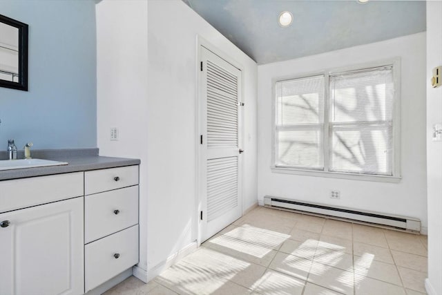 interior space with light tile patterned floors, recessed lighting, a baseboard heating unit, a sink, and baseboards