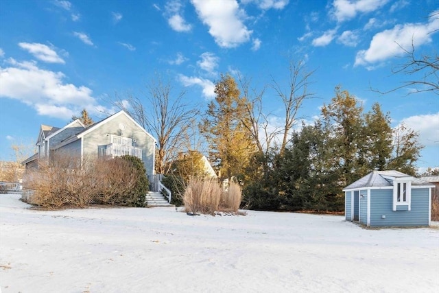 snowy yard with a balcony, a storage unit, and an outbuilding