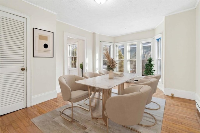 dining space featuring a textured ceiling, baseboards, light wood-style flooring, and crown molding