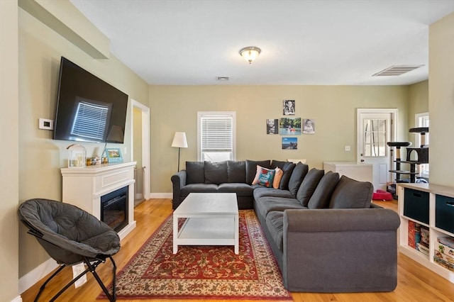 living area featuring visible vents, baseboards, light wood-style floors, and a glass covered fireplace