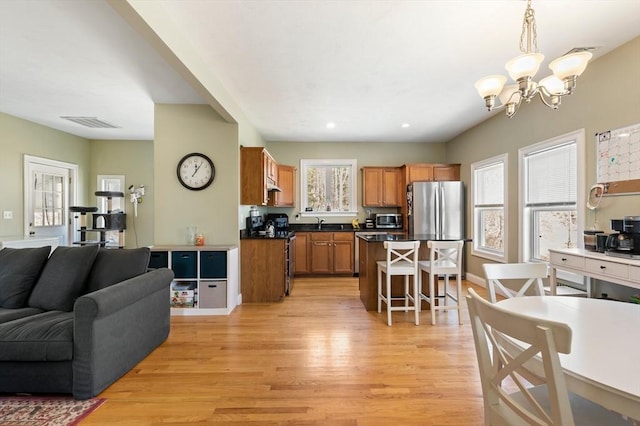 kitchen with light wood-type flooring, a breakfast bar, open floor plan, appliances with stainless steel finishes, and brown cabinets