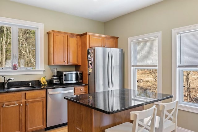 kitchen with dark stone countertops, a sink, stainless steel appliances, a kitchen bar, and brown cabinets