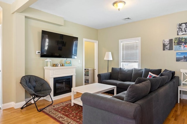 living area with visible vents, light wood-type flooring, baseboards, and a glass covered fireplace