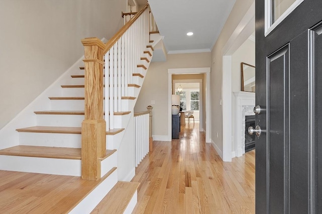 foyer entrance with baseboards, light wood-style flooring, a fireplace, recessed lighting, and crown molding