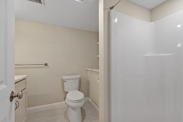 bathroom featuring baseboards, toilet, walk in shower, and vanity