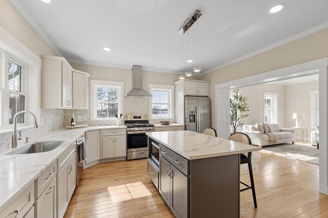 kitchen with wall chimney range hood, a breakfast bar, light wood-style flooring, stainless steel appliances, and a sink