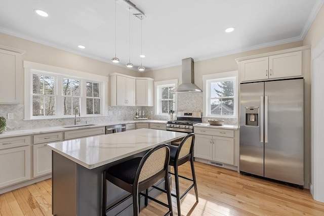 kitchen featuring a sink, stainless steel appliances, ornamental molding, and wall chimney range hood