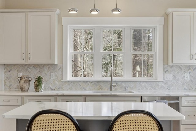 kitchen featuring tasteful backsplash, light stone counters, hanging light fixtures, white cabinets, and a sink