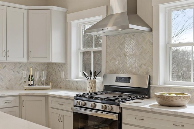 kitchen with white cabinets, wall chimney exhaust hood, gas stove, and tasteful backsplash