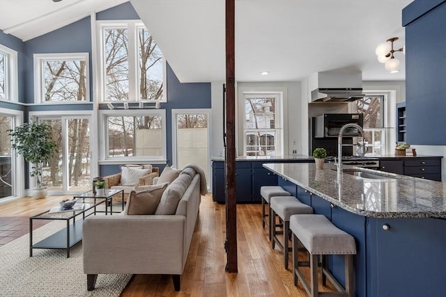 kitchen with blue cabinetry, a breakfast bar, lofted ceiling, and dark stone countertops