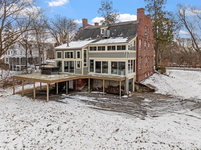 snow covered property featuring a deck, a sunroom, and a hot tub