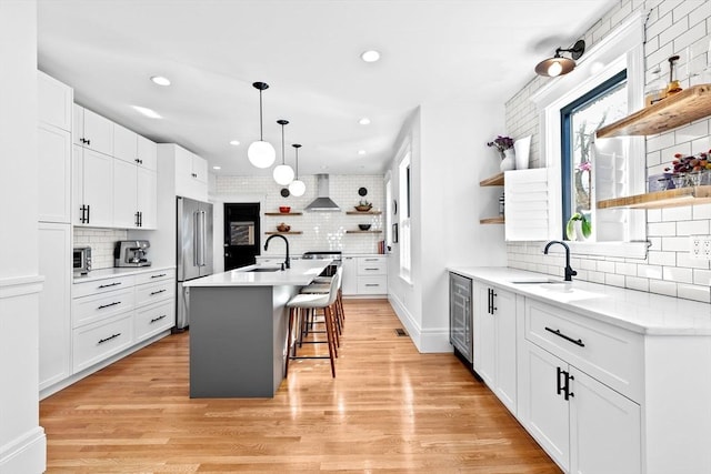 kitchen with open shelves, wall chimney exhaust hood, beverage cooler, and a sink