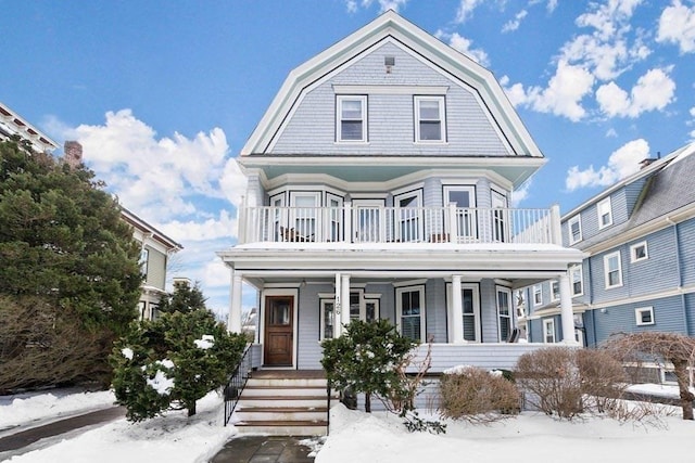 view of front facade featuring covered porch, a gambrel roof, and a balcony