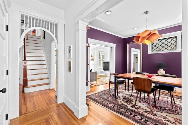 dining area featuring ornate columns, arched walkways, ornamental molding, stairs, and parquet flooring