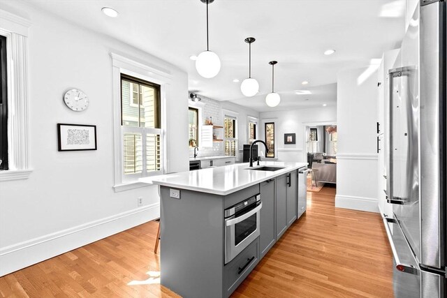 kitchen with gray cabinets, a sink, light wood-style floors, appliances with stainless steel finishes, and light countertops