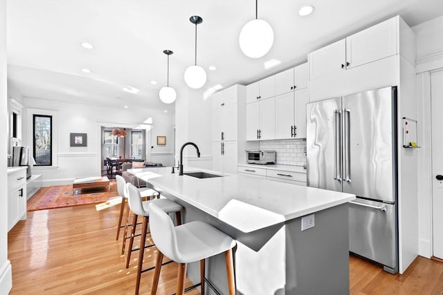 kitchen with high end fridge, a sink, backsplash, white cabinets, and light wood finished floors