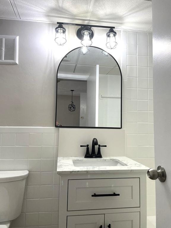 bathroom featuring vanity, toilet, tile walls, and a textured ceiling