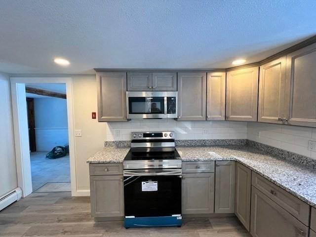 kitchen featuring stainless steel appliances, a baseboard heating unit, light stone counters, and decorative backsplash