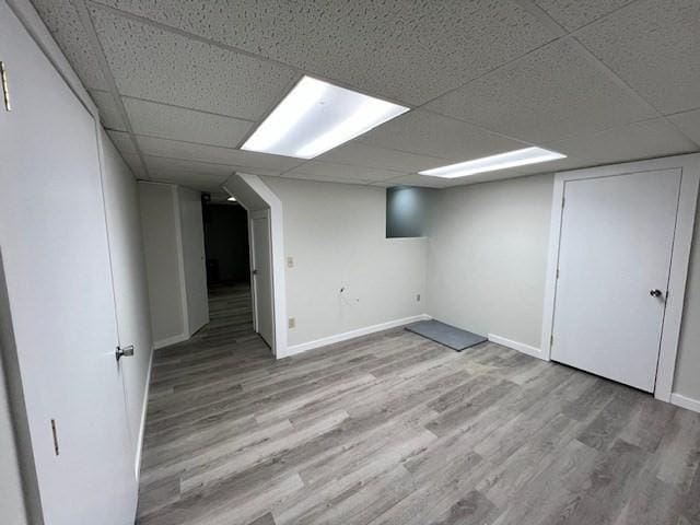 finished basement with a paneled ceiling, baseboards, and light wood finished floors