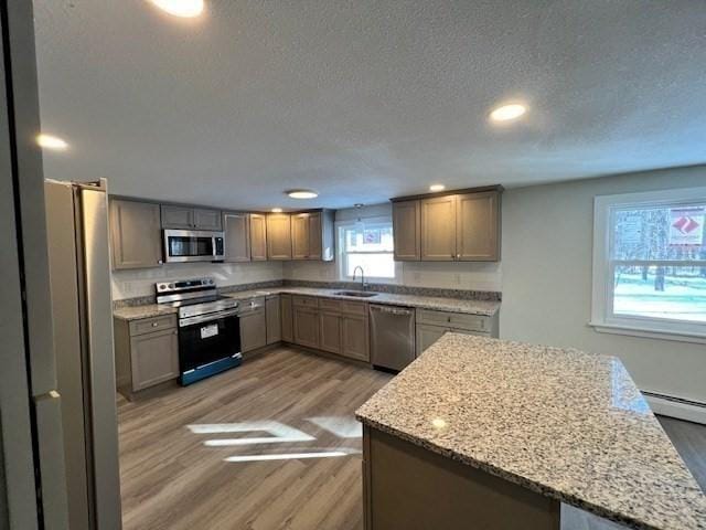 kitchen with light stone countertops, wood finished floors, a sink, appliances with stainless steel finishes, and a center island