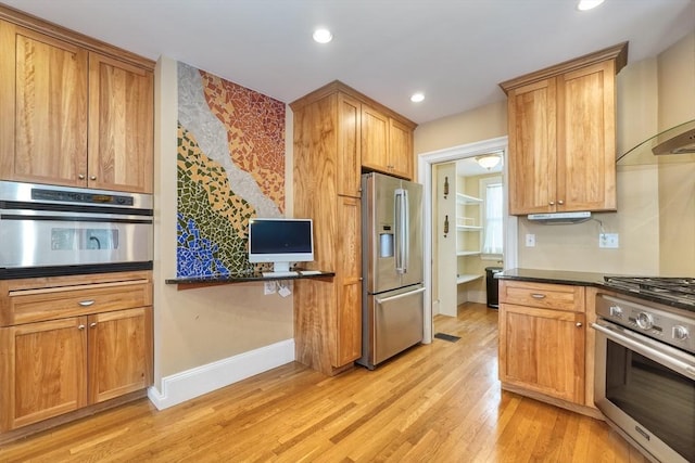 kitchen featuring dark stone countertops, light hardwood / wood-style floors, wall chimney exhaust hood, and appliances with stainless steel finishes