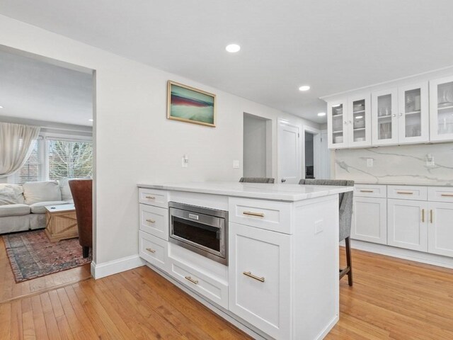 kitchen featuring stainless steel microwave, white cabinetry, a breakfast bar area, decorative backsplash, and light wood-type flooring