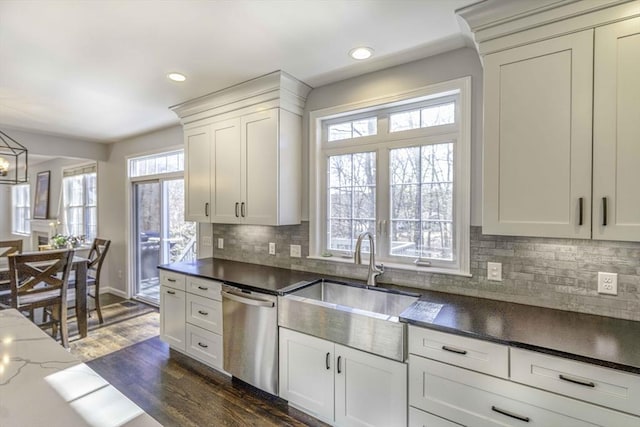 kitchen featuring dark stone countertops, dark wood-style floors, a sink, dishwasher, and tasteful backsplash