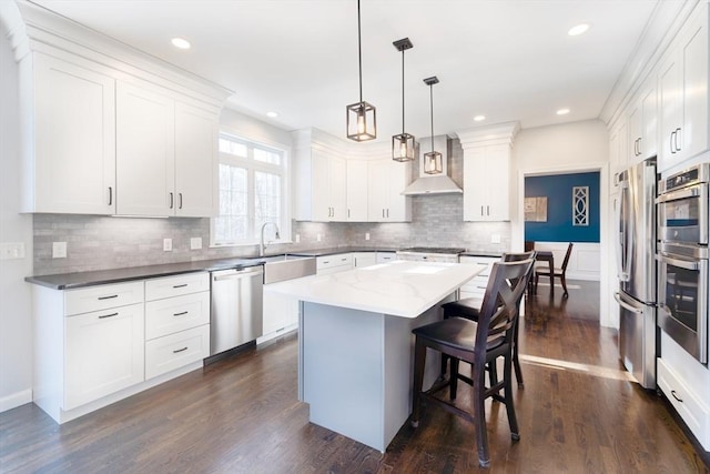 kitchen with dark wood-type flooring, appliances with stainless steel finishes, a kitchen breakfast bar, wall chimney exhaust hood, and a center island