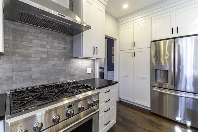 kitchen with dark wood finished floors, stainless steel appliances, wall chimney exhaust hood, white cabinets, and decorative backsplash