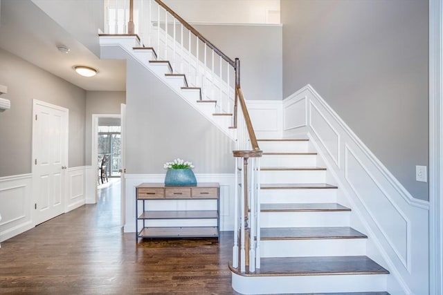 stairway with a wainscoted wall, a decorative wall, a towering ceiling, and wood finished floors