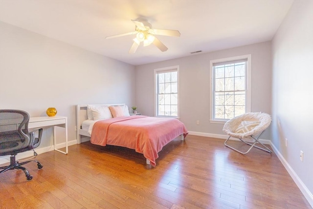 bedroom with ceiling fan, wood finished floors, visible vents, and baseboards