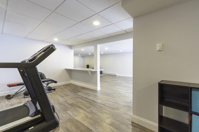 exercise room with wood finished floors, baseboards, a baseboard radiator, recessed lighting, and a drop ceiling