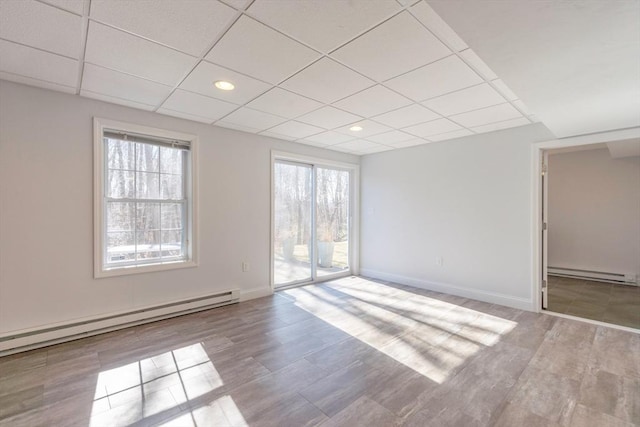 unfurnished room with a healthy amount of sunlight, a baseboard heating unit, and a paneled ceiling