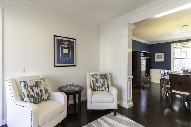 sitting room featuring wood finished floors, an inviting chandelier, decorative columns, ornamental molding, and wainscoting