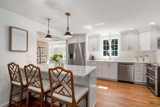 kitchen with decorative backsplash, stainless steel appliances, light wood finished floors, light countertops, and a kitchen bar