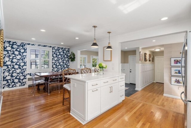 kitchen featuring white cabinets, wallpapered walls, light countertops, crown molding, and light wood-style flooring