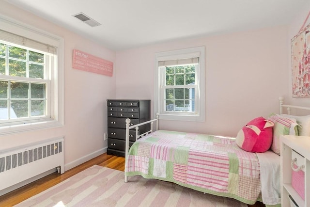 bedroom featuring radiator, wood finished floors, visible vents, and multiple windows