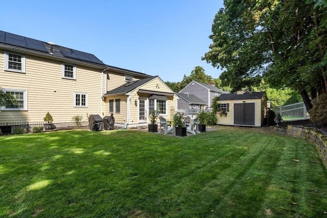 back of property featuring roof mounted solar panels, a fenced backyard, a storage shed, an outdoor structure, and a lawn