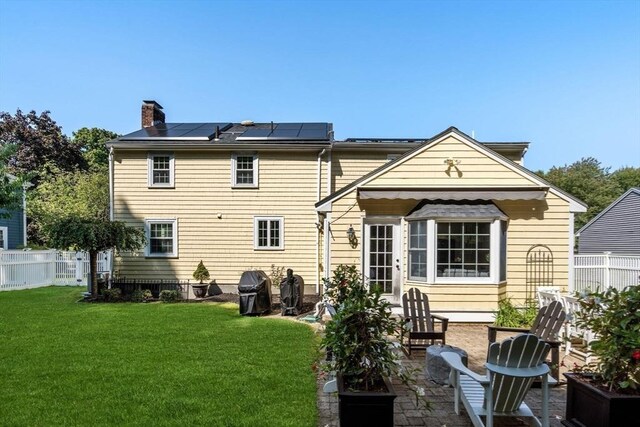 back of property featuring a chimney, fence, a patio area, a lawn, and roof mounted solar panels