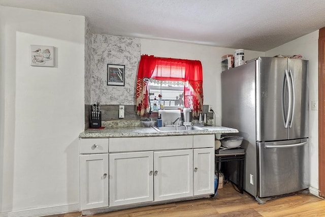 kitchen featuring white cabinets, sink, stainless steel fridge, and light wood-type flooring