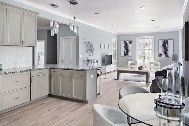 kitchen with ornamental molding, decorative light fixtures, light stone counters, and light hardwood / wood-style flooring