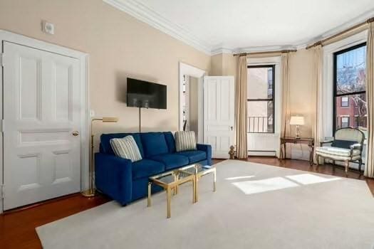 living area with a baseboard heating unit, crown molding, and wood finished floors