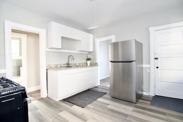 kitchen with sink, white cabinetry, stainless steel refrigerator, and black range with gas stovetop