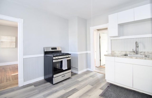 kitchen featuring sink, white cabinets, stainless steel range with gas stovetop, and light wood-type flooring