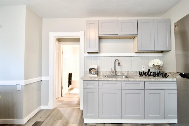 kitchen featuring light hardwood / wood-style floors, sink, stainless steel refrigerator, light stone counters, and gray cabinetry